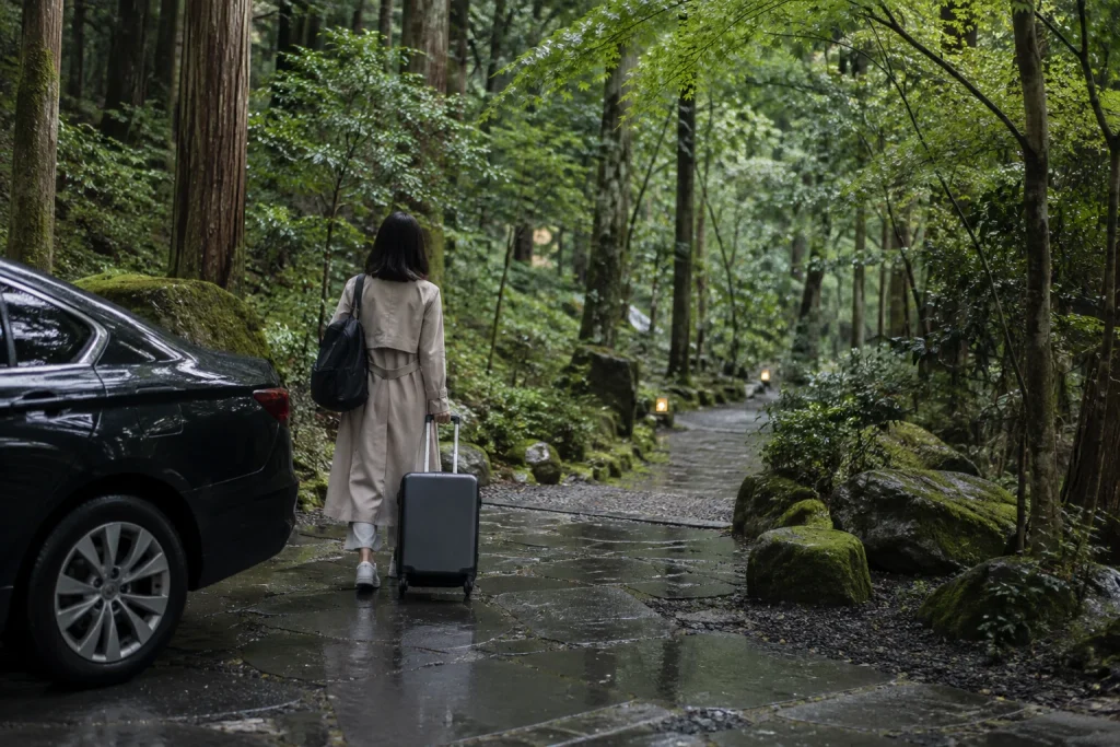 雨上がりの森で車を降りキャリーケースを引いて石径へ進む女性