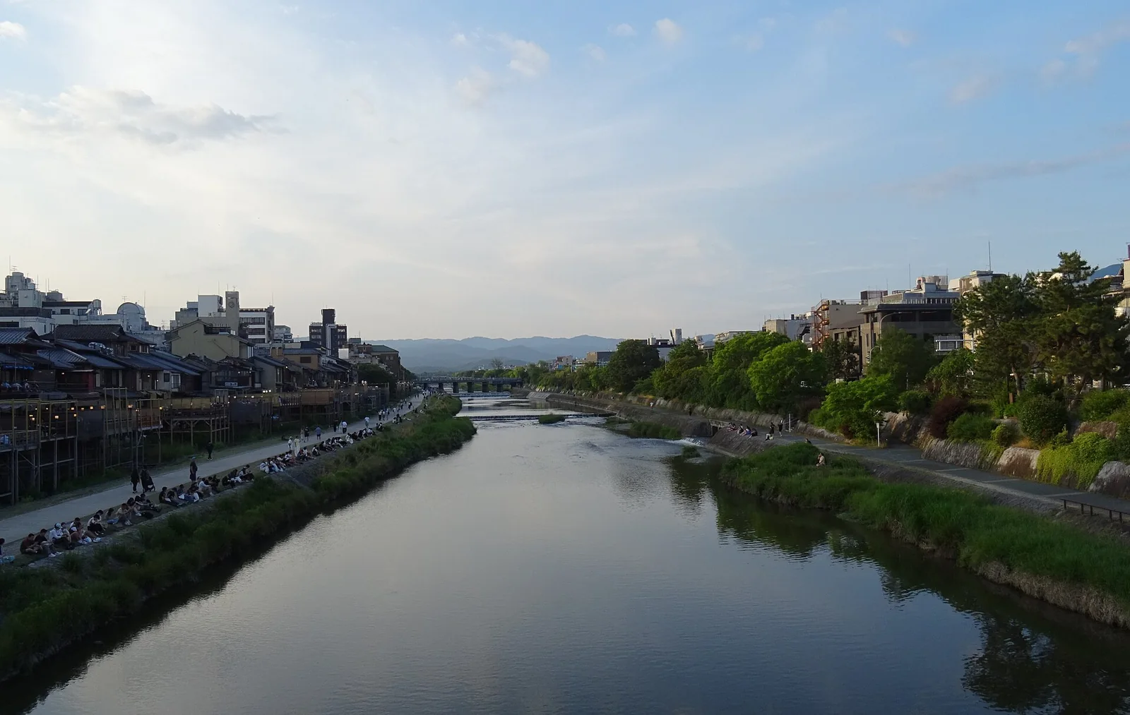 夕焼け空の下で鴨川沿いに座る人々と京都の町並み