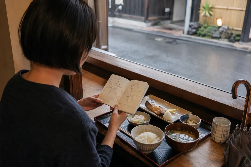 京都の食事処で昼食と次の行き先をノートで確かめる一人旅の女性
