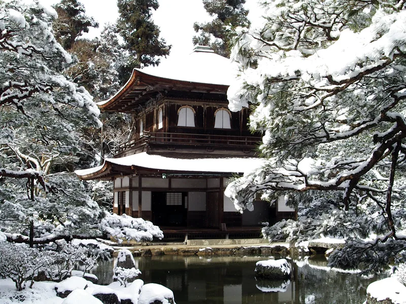 雪をかぶった庭と木々の向こうに立つ銀閣寺観音殿