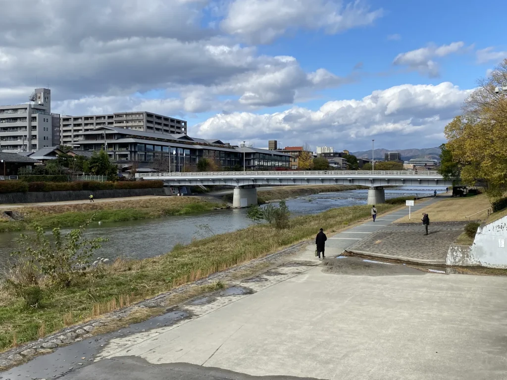 青空と雲の下で鴨川に架かる二条大橋と川沿いの歩道