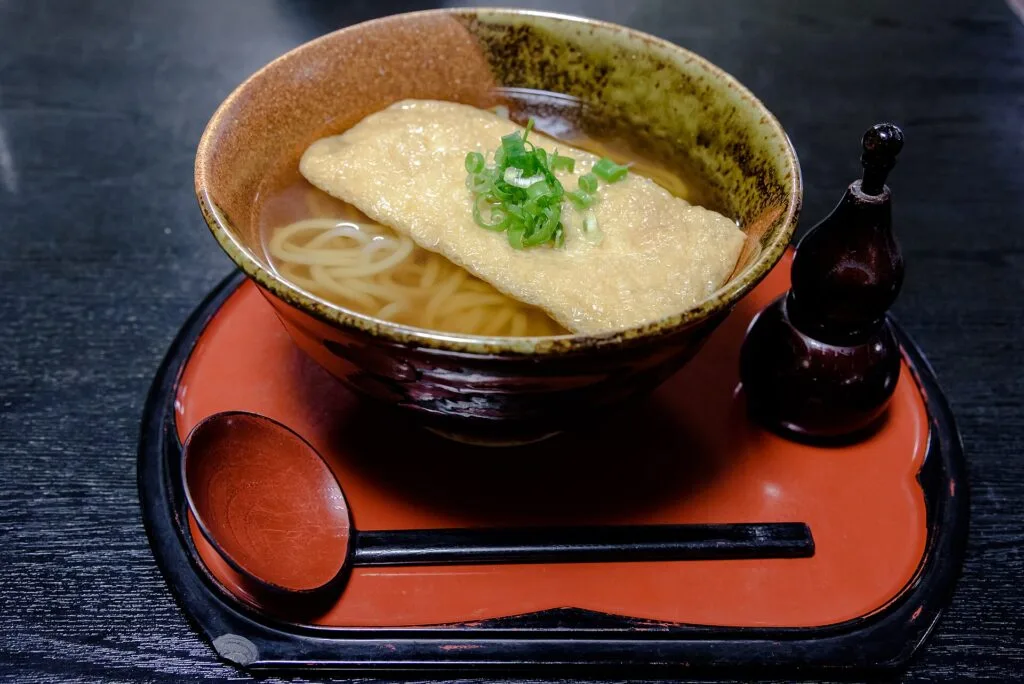 大きな油揚げと青ねぎをのせた温かいうどん