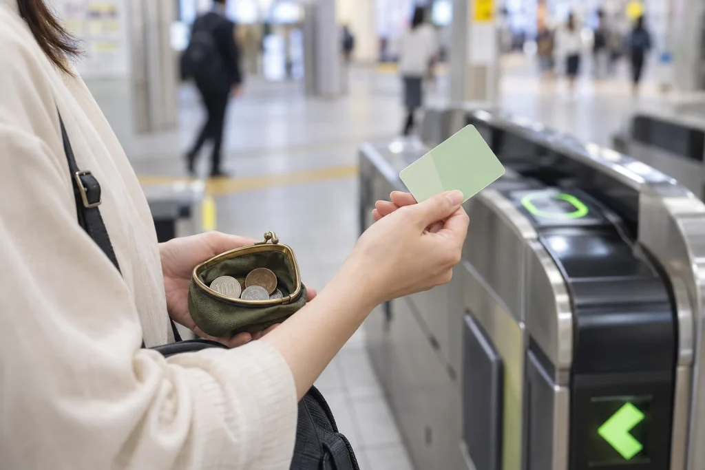 駅の改札前で無地の交通系ICカードと少額の現金を用意する女性の手元