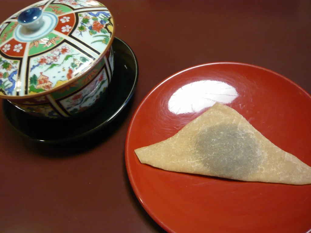 朱色の皿に置かれた生八ツ橋と蓋付きの湯呑み