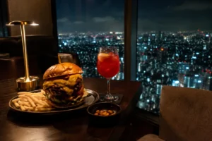 高層階の窓際に、一人分の大きなチーズバーガーと赤いカクテルが置かれている