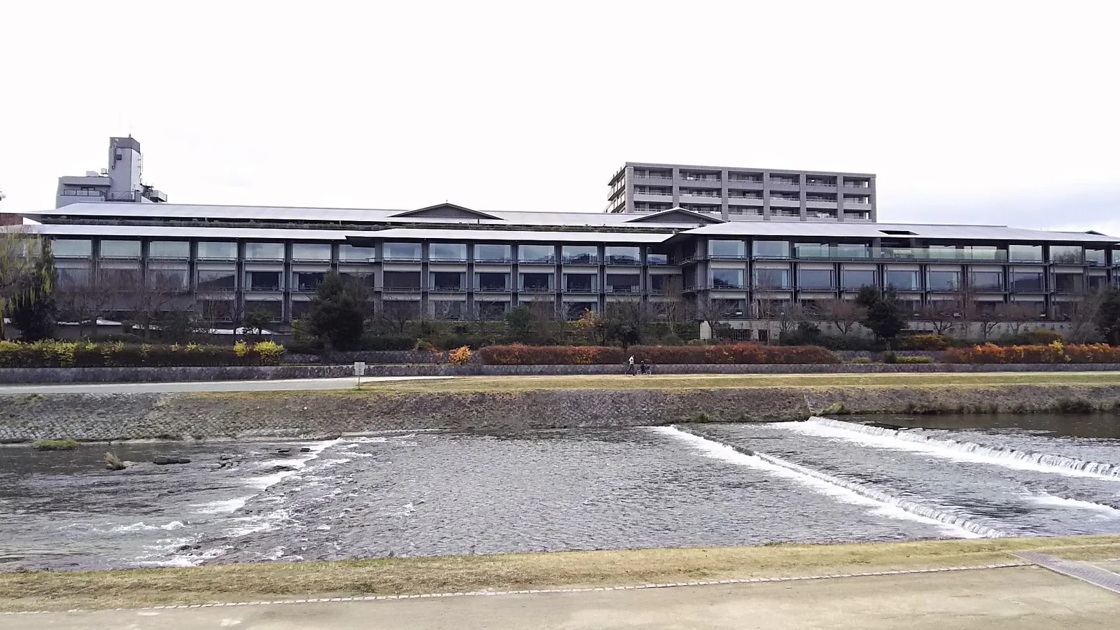 鴨川と低い堰の向こうに横長に建つザ・リッツ・カールトン京都