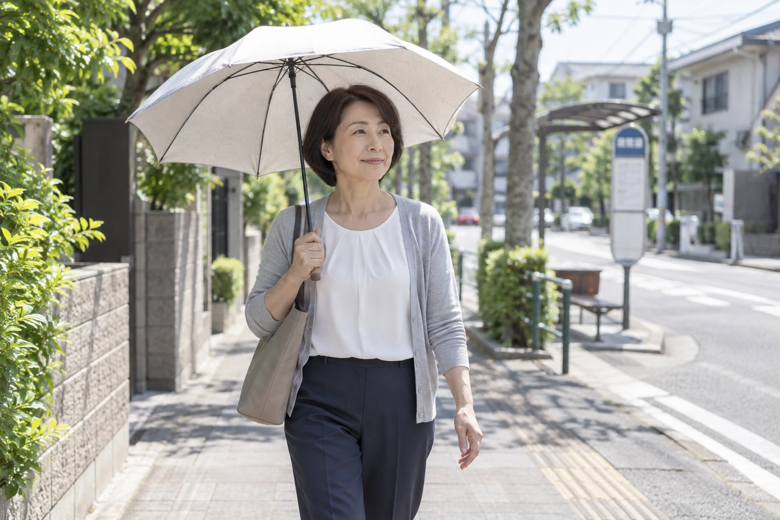 夏の朝、木陰と日なたのある住宅街を日傘を差して歩く女性のイメージ