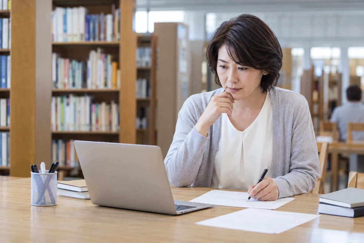 求人サイト以外の仕事探しを図書館で調べる日本人女性の編集写真