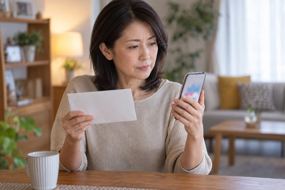友達の住所を確認するか考える日本人女性と白い封筒の編集写真