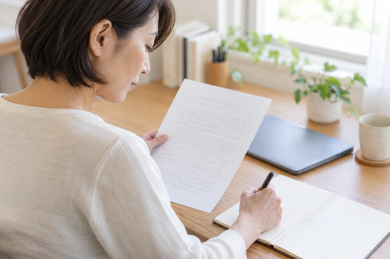 公的資料を読みながら手元のノートに確認点を書き留める人。数値の対象と限界を確認する場面