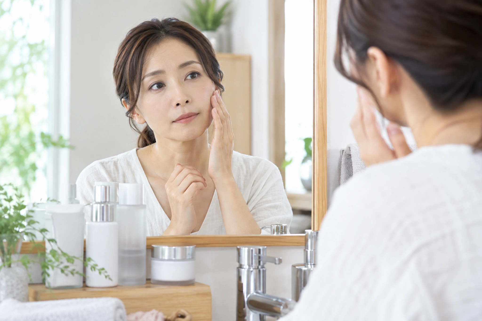 鏡の前で肌の手入れを始めるか考える女性