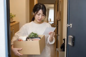 一人暮らしの女性が宅配弁当の箱と案内を確認している様子