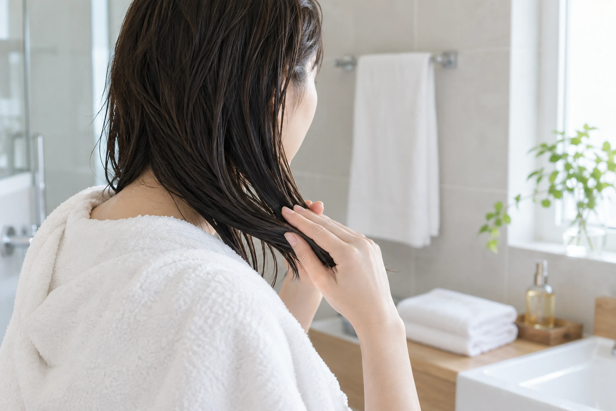 タオルドライ後の髪の中間から毛先へヘアオイルをなじませる女性