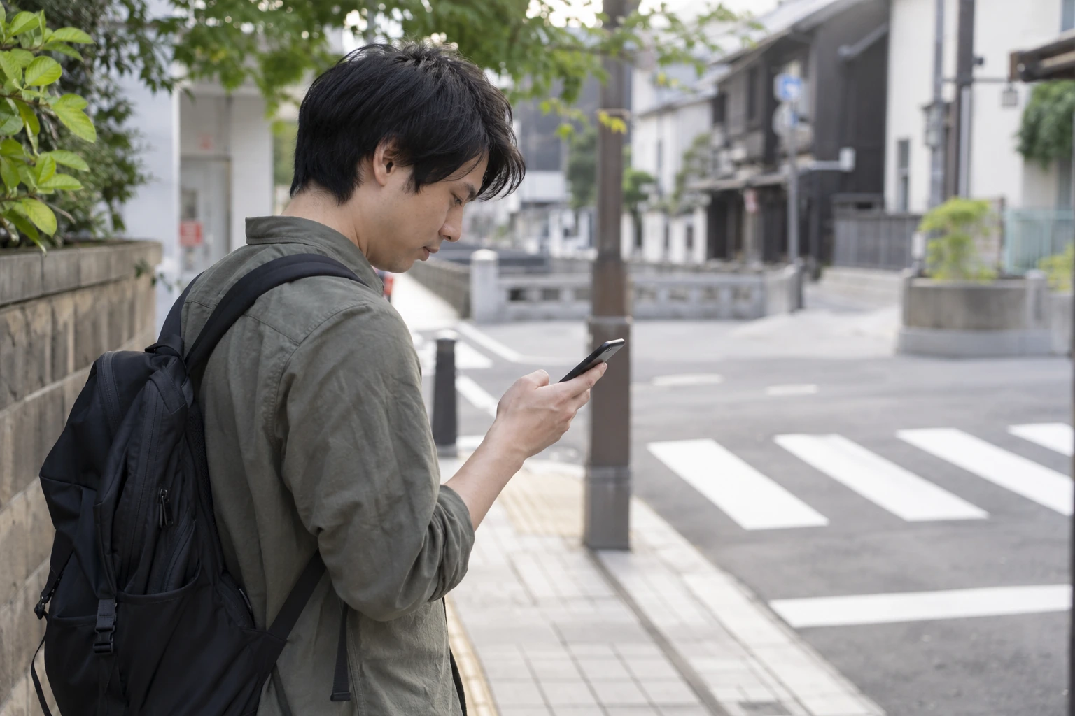 通行の妨げにならない場所で立ち止まりスマートフォンで道順を確認する男性