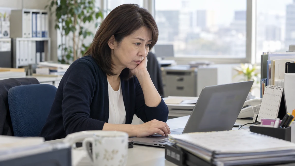 共有連絡から漏れた納期変更に気づき、業務の支障を確認する日本人女性の編集イメージ
