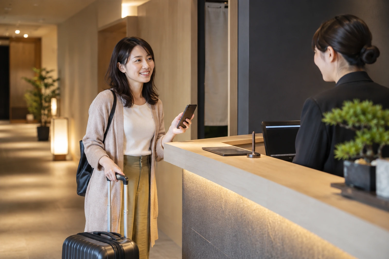 予約情報を受付で提示する一人旅の女性とスタッフの利用イメージ