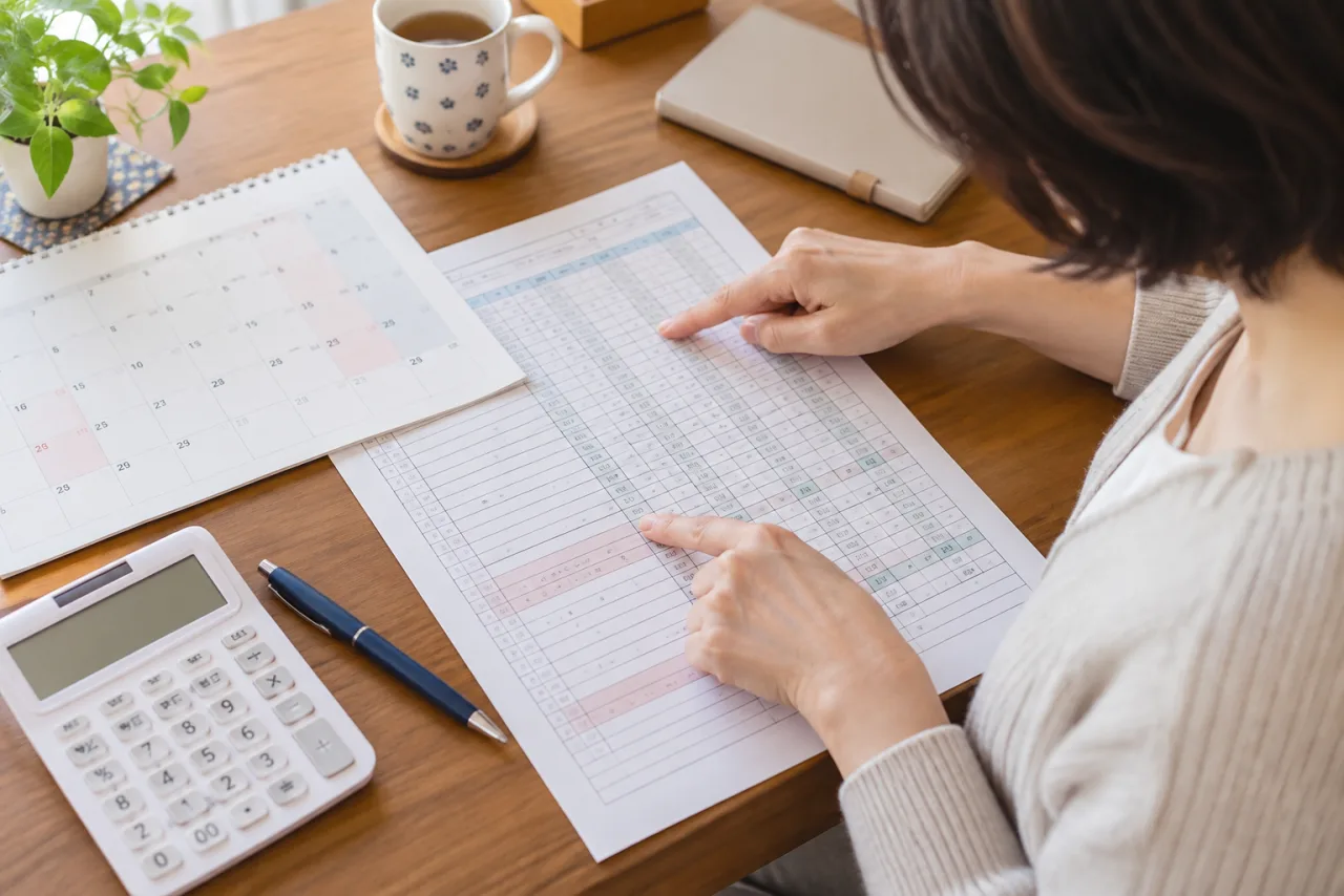 日本人の一人暮らしの女性が勤務表と給与明細を机に並べて働き方を見直す